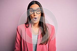 Young beautiful brunette businesswoman wearing jacket and glasses over pink background afraid and shocked with surprise