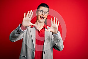 Young beautiful brunette businesswoman wearing jacket and glasses over red background afraid and terrified with fear expression