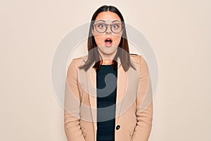 Young beautiful brunette businesswoman wearing jacket and glasses over white background afraid and shocked with surprise