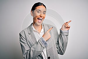 Young beautiful brunette businesswoman wearing jacket standing over white background smiling and looking at the camera pointing