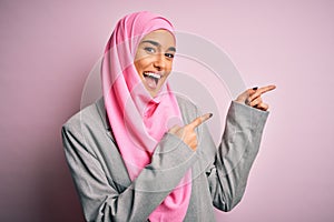 Young beautiful brunette businesswoman wearing pink muslim hijab and business jacket smiling and looking at the camera pointing