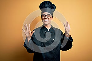 Young beautiful brunette chef woman wearing cooker uniform and hat over yellow background showing and pointing up with fingers