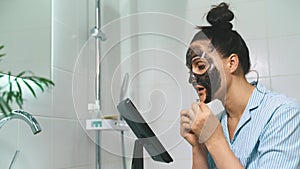 A young, beautiful brunette cleans her face in the bathroom with a mask.