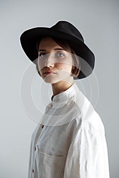 Young beautiful brunette girl in black hat over white background.