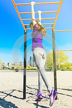 Young beautiful brunette girl in blue t-shirt climbing a horizontal ladder in the park.