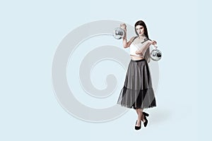 Young beautiful brunette girl in dark box pleated midi skirt posing in studio. Woman balancing holding two disco balls