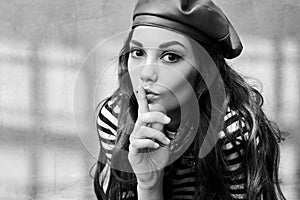 Young beautiful brunette girl dressed in retro vintage style in the old european city makes a hush gesture in black and