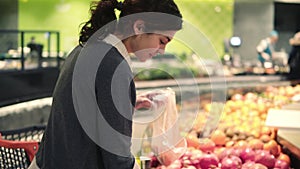 Young beautiful brunette girl in her 20`s picking out tangerines into a plastic bag at the fruit and vegetable aisle in