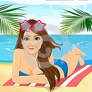 Young beautiful brunette girl lying on a beach towel