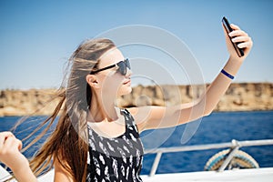 Young beautiful brunette girl making selfie using phone while relaxing on the luxury yacht