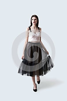Young beautiful brunette girl in waving dark box pleated midi skirt posing in studio. Woman dancing or making a step.