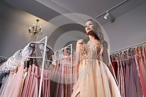 Young beautiful brunette girl wearing a full-length beige yellow champaign chiffon slit prom ball gown decorated with