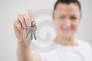 A young beautiful brunette girl in a white T-shirt holds in her hands the keys to a new home, against the background of
