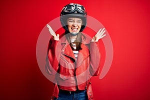 Young beautiful brunette motocyclist woman wearing motorcycle helmet and red jacket celebrating mad and crazy for success with