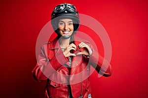 Young beautiful brunette motorcyclist woman wearing motorcycle helmet and red jacket smiling in love showing heart symbol and