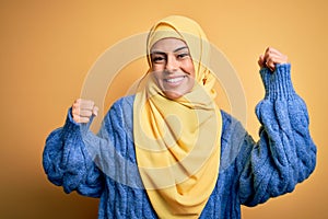 Young beautiful brunette muslim woman wearing arab hijab over isolated yellow background Dancing happy and cheerful, smiling