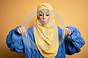 Young beautiful brunette muslim woman wearing arab hijab over isolated yellow background Pointing down with fingers showing
