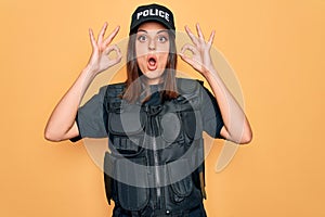 Young beautiful brunette policewoman wearing police uniform bulletproof and cap looking surprised and shocked doing ok approval