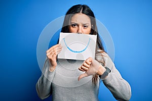 Young beautiful brunette positive woman holding card with smile emotion on mouth with angry face, negative sign showing dislike