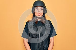 Young beautiful brunette soldier woman wearing bulletproof and security helmet afraid and shocked with surprise expression, fear