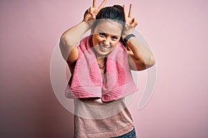 Young beautiful brunette sportswoman wearing sportswear and towel over pink background Posing funny and crazy with fingers on head