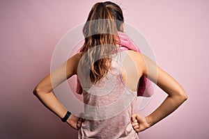 Young beautiful brunette sportswoman wearing sportswear and towel over pink background standing backwards looking away with arms