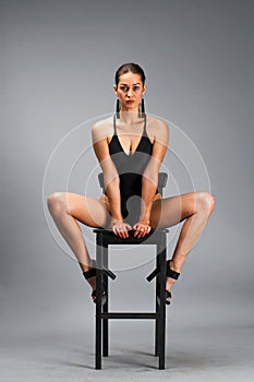 Young beautiful brunette woman in a black solid swimsuit sitting on a chair in the studio