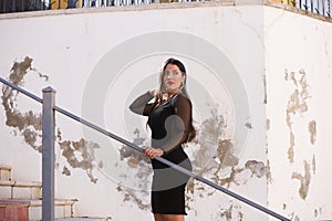 Young, beautiful brunette woman is dressed elegantly in a black dress with transparencies. The girl is climbing a ladder in the photo