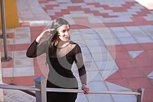 Young, beautiful brunette woman is dressed elegantly in a black dress with transparencies. The girl is climbing a ladder in the photo