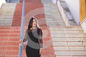 Young, beautiful brunette woman is dressed elegantly in a black dress with transparencies. The girl is walking down a staircase in photo