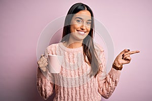 Young beautiful brunette woman drinking cup of coffee over isolated pink background very happy pointing with hand and finger to