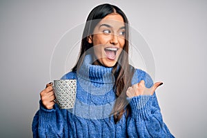 Young beautiful brunette woman drinking cup of coffee over isolated white background pointing and showing with thumb up to the