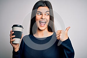 Young beautiful brunette woman drinking cup of coffee over isolated white background pointing and showing with thumb up to the