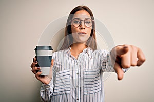 Young beautiful brunette woman drinking cup of takeaway coffe over white background pointing with finger to the camera and to you,