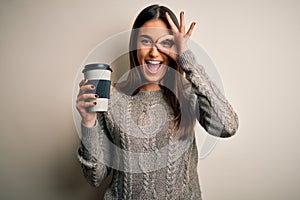 Young beautiful brunette woman drinking glass of coffee over isolated white background with happy face smiling doing ok sign with