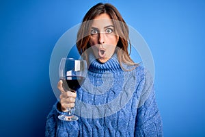 Young beautiful brunette woman drinking glass of red wine over isolated blue background scared in shock with a surprise face,