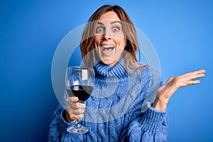 Young beautiful brunette woman drinking glass of red wine over isolated blue background very happy and excited, winner expression