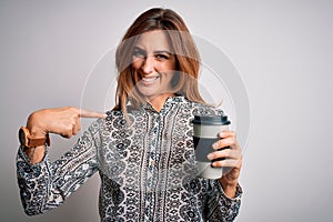 Young beautiful brunette woman drinking glass of takeaway coffe over white background with surprise face pointing finger to