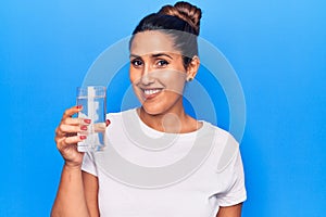 Young beautiful brunette woman drinking glass of water looking positive and happy standing and smiling with a confident smile