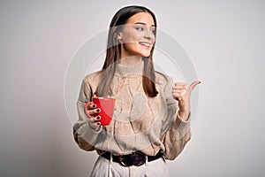 Young beautiful brunette woman drinking red cup of coffee over isolated white background pointing and showing with thumb up to the