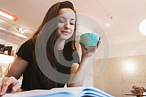 Young beautiful brunette woman drinks hot coffee in the cafe looks concentrated checking her planner