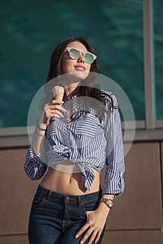 Young, beautiful brunette woman eating a pink ice cream in a waffle horn. She`s in a good mood She wears glasses with dark glasse