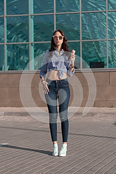 Young, beautiful brunette woman eating a pink ice cream in a waffle horn. She`s in a good mood She wears glasses with dark glasse