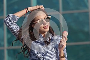 Young, beautiful brunette woman eating pink ice cream in a waffle horn. She`s in a good mood She wears glasses with dark glasses,