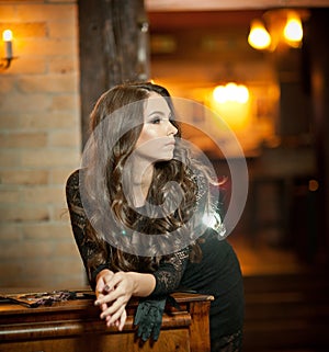 Young beautiful brunette woman in elegant black dress standing near a vintage piano. Sensual romantic lady with long dark hair