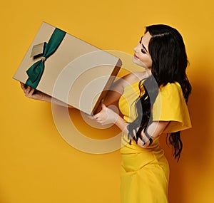 Young beautiful brunette woman got present gift box with green ribbon for birthday happy surprised in trendy yellow dress