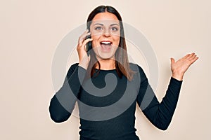 Young beautiful brunette woman having conversation talking on the smartphone celebrating victory with happy smile and winner