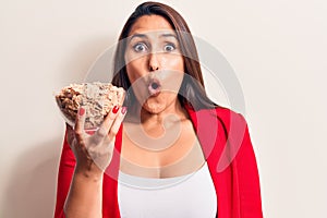 Young beautiful brunette woman holding bowl of cornflakes cereal scared and amazed with open mouth for surprise, disbelief face