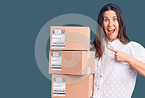 Young beautiful brunette woman holding delivery cardboard package smiling happy pointing with hand and finger