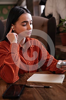 Young beautiful brunette woman listening to music holds a wireless earphone in her ear enjoying a new song while sitting